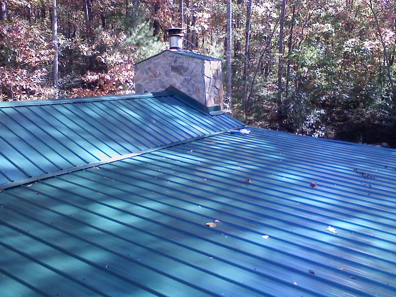 New green metal roof and stone chimney surrounded by autumn woods in Waterloo