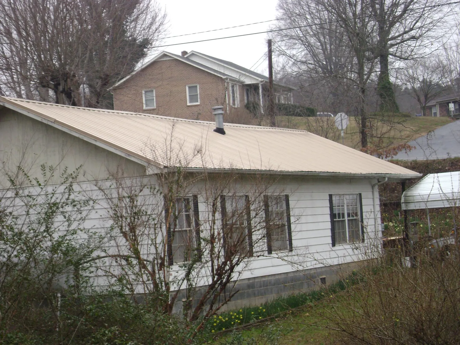 Tan metal roof on a white sided house set into a hillside — Commercial Roofing by Roofing Brothers in Waterloo