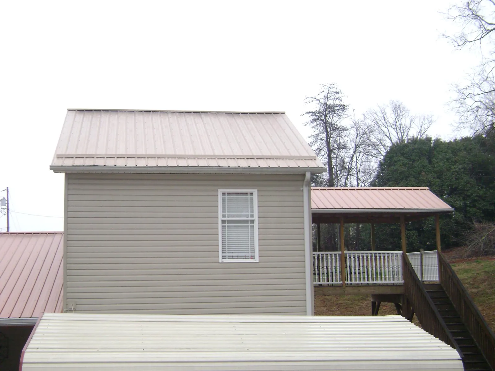 Tan metal roofs on a two story addition and attached porch, from a Roof Replacement job in Waterloo